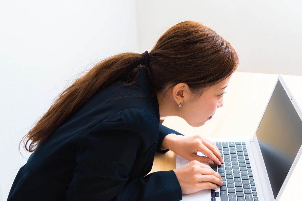 机の上で前のめりになってパソコンの画面をのぞき込む女性